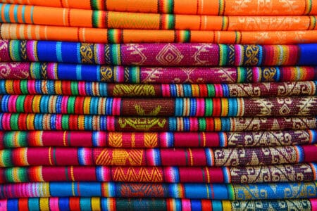 Bunte handgewebte Stoffe mit traditionellen Mustern auf dem Kunsthandwerksmarkt Otavalo in Ecuador – farbenfrohe Textilien aus den Anden.